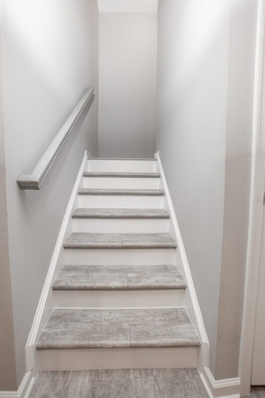 Basement staircase with gray treads, white risers and wall-mounted handrail
