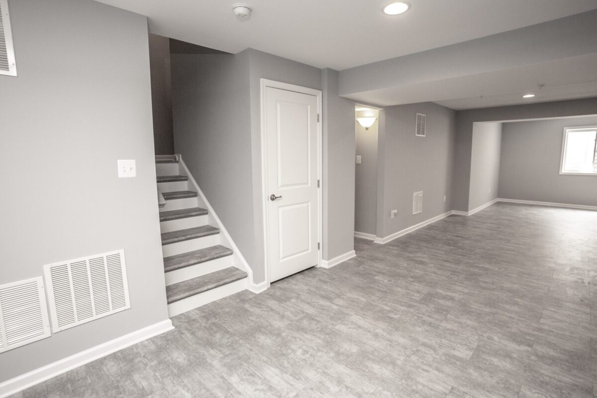 Open finished basement with staircase, gray plank flooring and recessed lights
