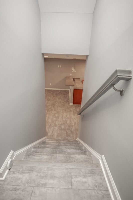 View down a finished basement staircase with tile flooring and handrail