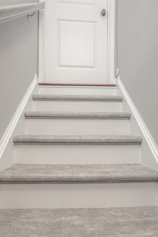 Basement stairs with gray treads leading up to a white door