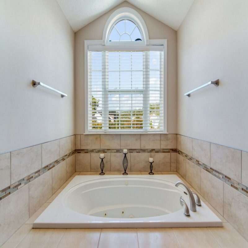 Drop-in jetted tub with tile surround beneath an arched window