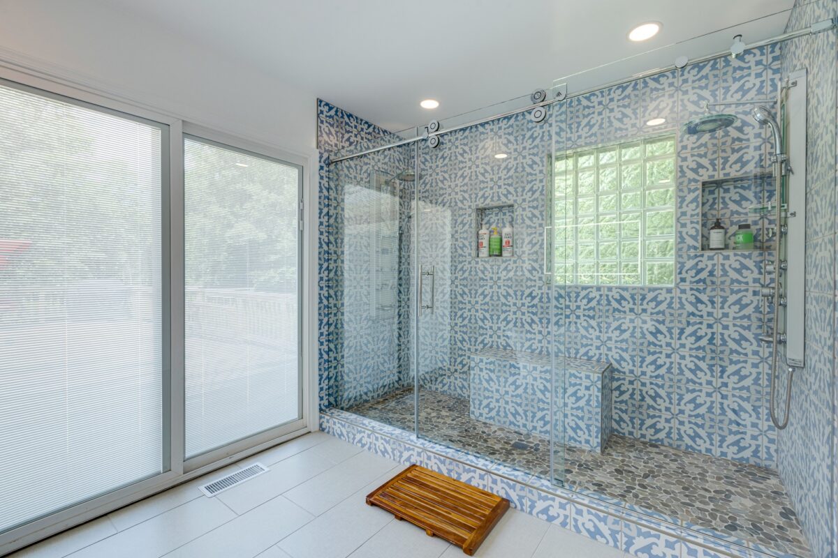 Large walk-in shower with blue patterned tile, glass block window and built-in bench