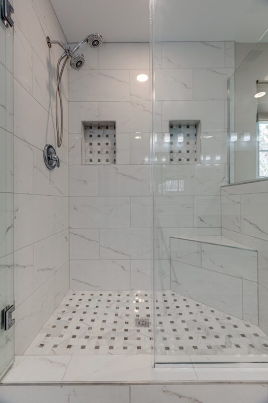 Walk-in shower with white marble-look tile, niches, bench and mosaic floor