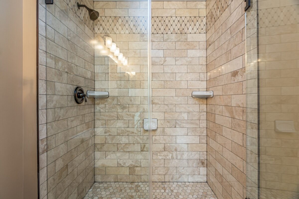 Walk-in shower with travertine-look subway tile and hexagon mosaic floor