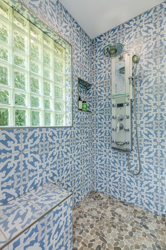 Blue patterned tile shower with pebble floor, bench and glass block window