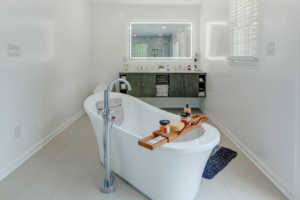 Freestanding tub with floor faucet and tub caddy facing a floating vanity with lighted mirror