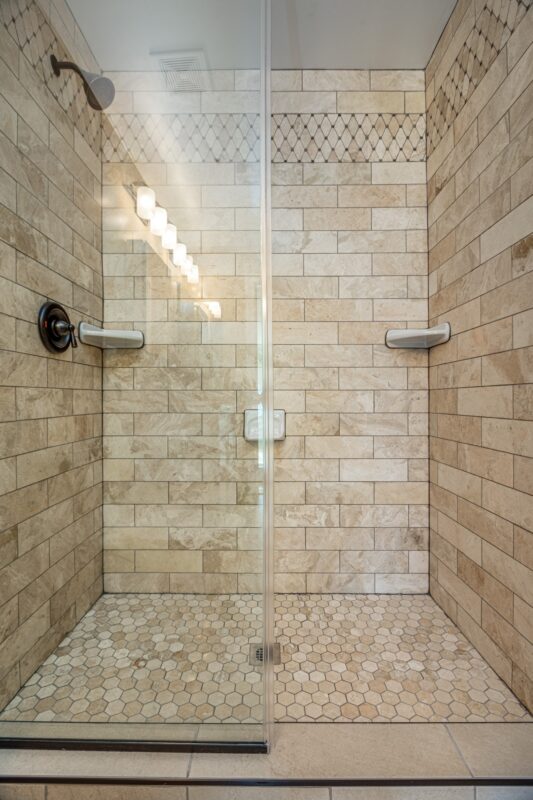 Travertine-look tile walk-in shower with frameless glass and hexagon mosaic floor