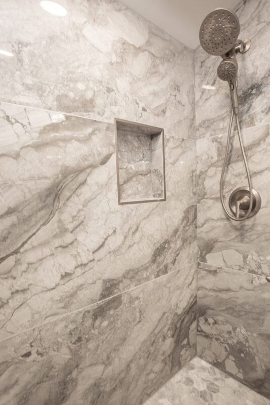 Marble-look tile shower wall with recessed niche and handheld showerhead