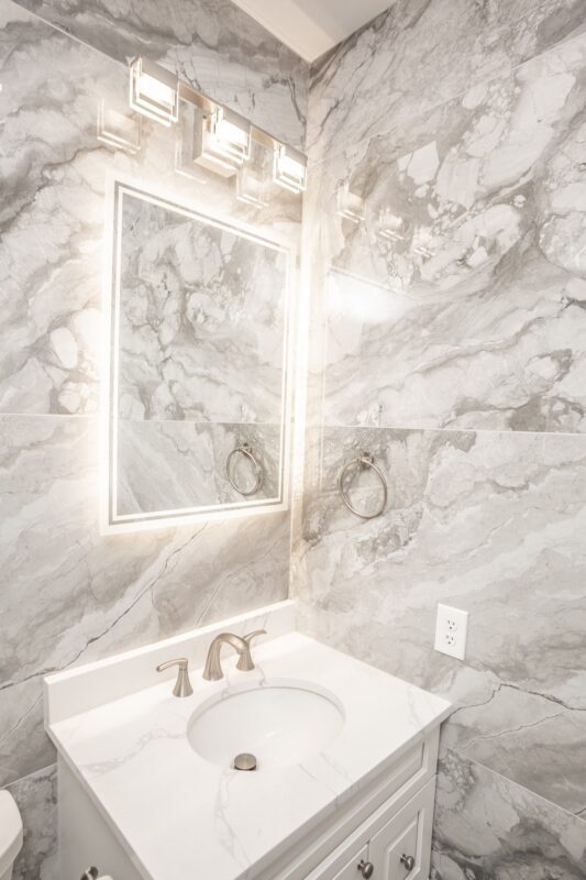 White vanity with lighted mirror and marble-look tile walls