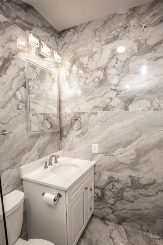 Small bathroom with white vanity, vanity light and marble-look tile walls