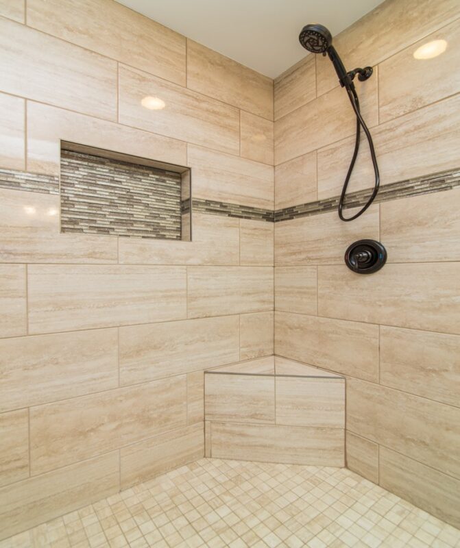 Walk-in shower with beige plank tile, mosaic niche and corner bench