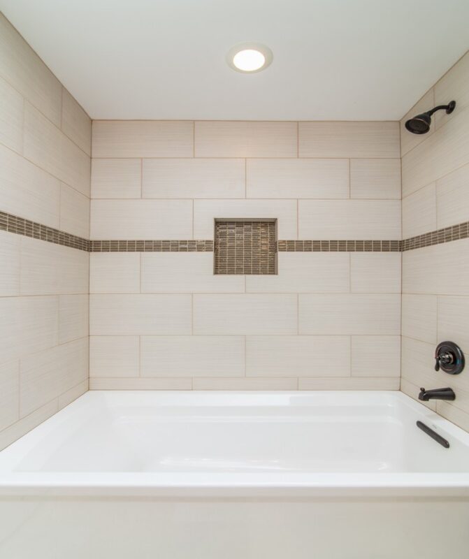 Bathtub with beige tile surround, mosaic accent band and niche