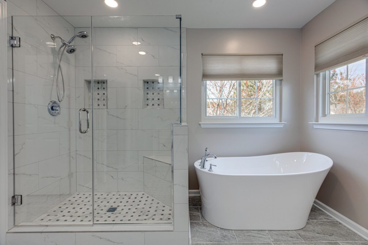 Glass walk-in shower with marble-look tile next to a freestanding tub