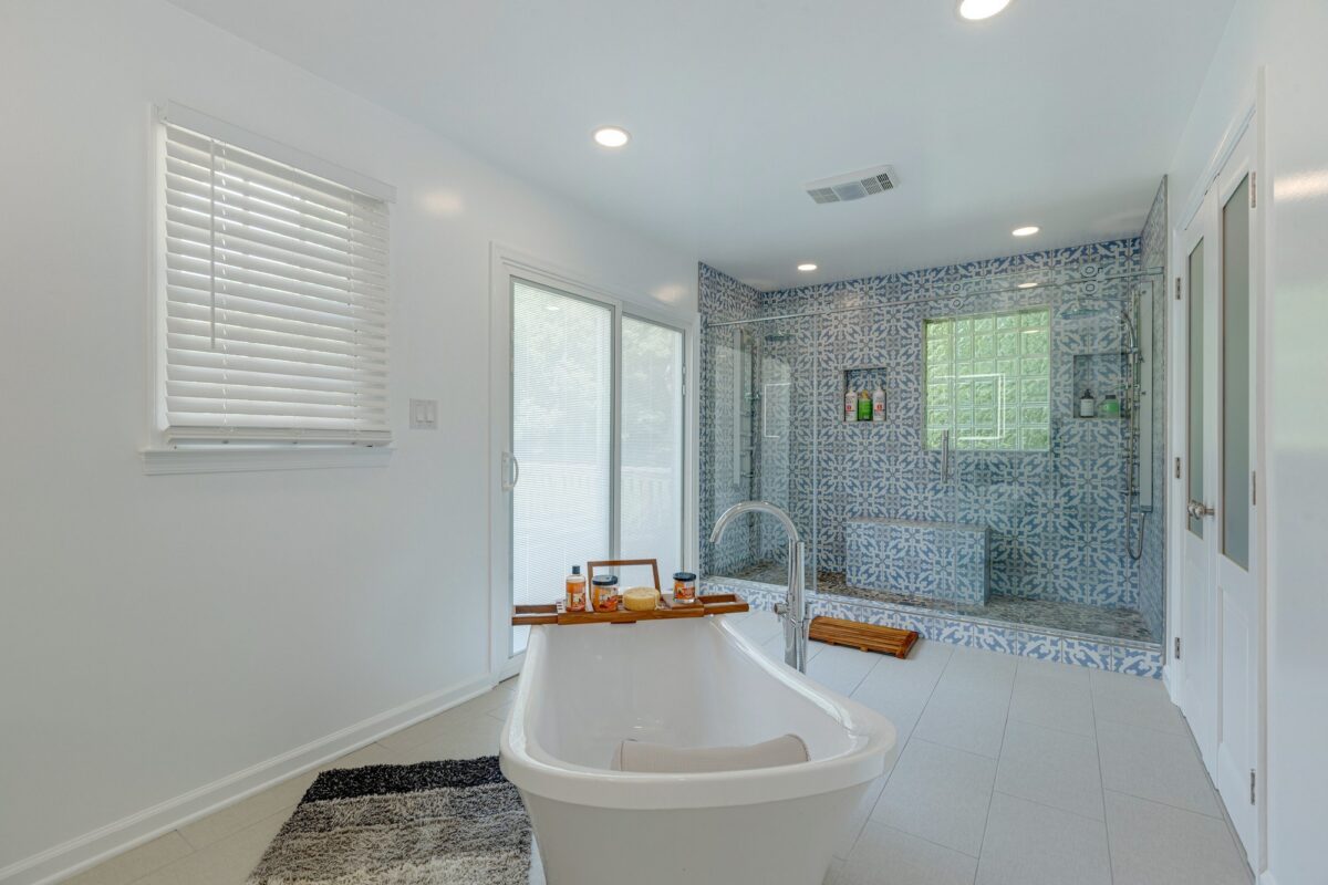 Freestanding tub in front of a blue patterned tile shower with glass block window