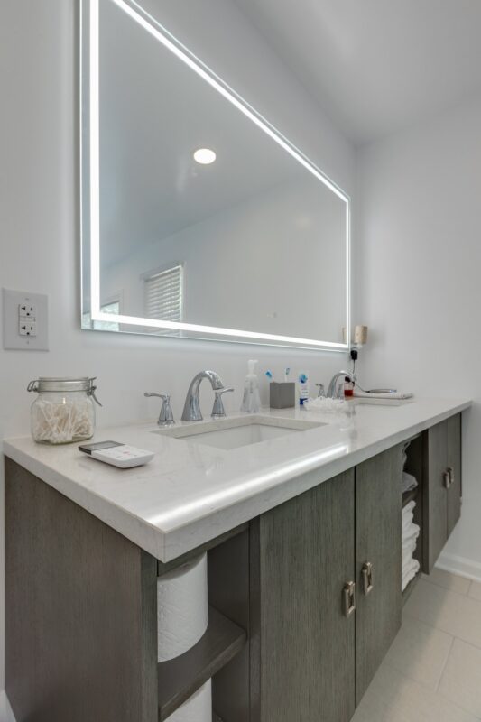 Floating gray vanity with quartz top, open shelves and lighted mirror