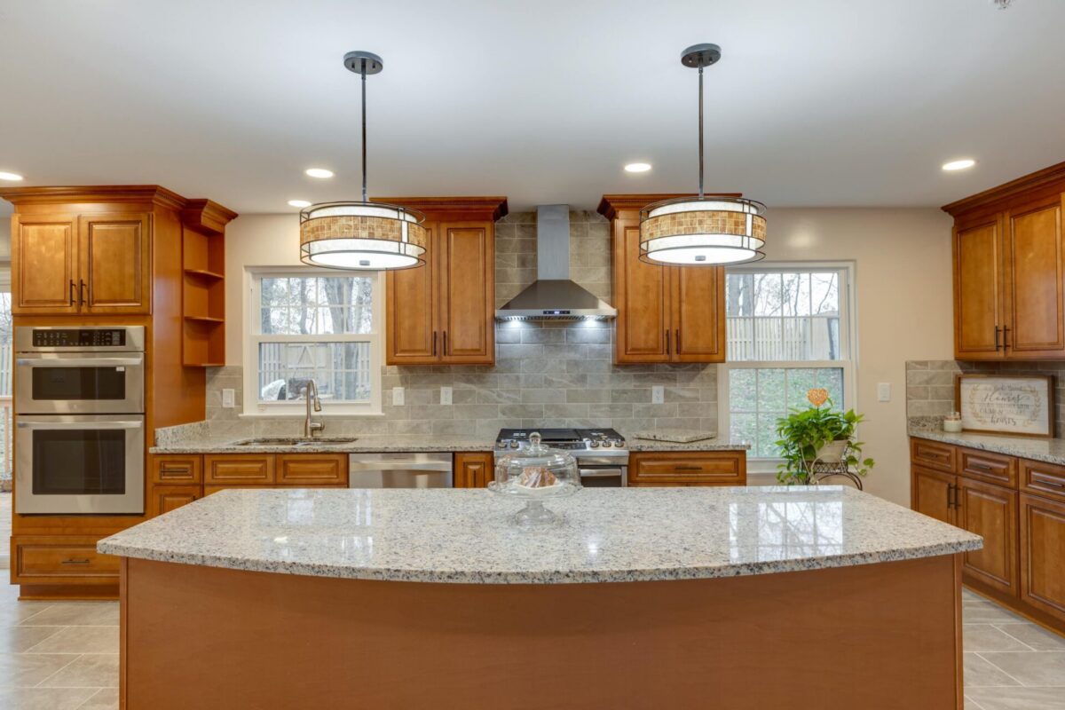 Kitchen with wood cabinets, granite island, double wall ovens and drum pendants