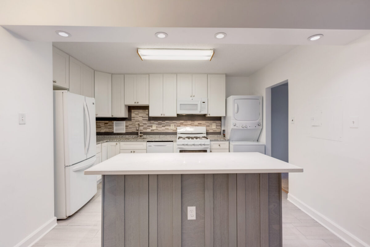 Kitchen with white cabinets, island and stacked washer and dryer
