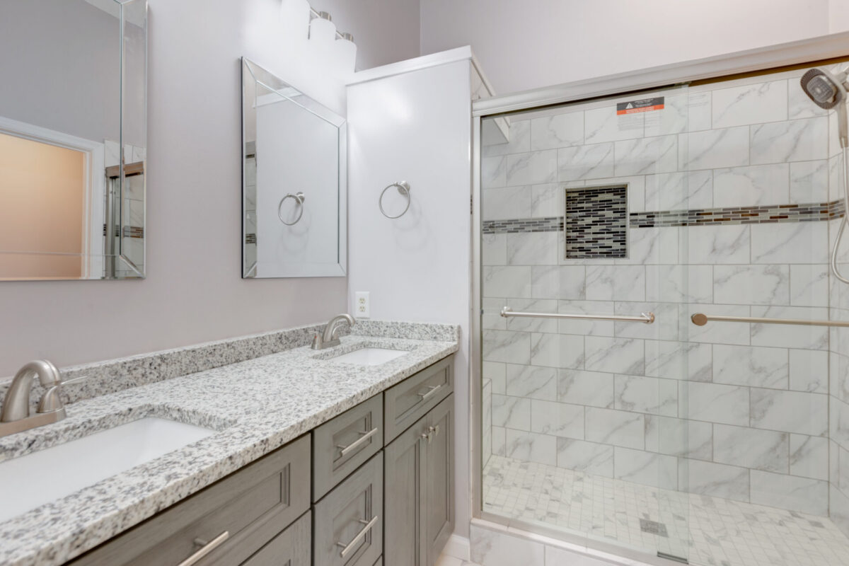 Gray vanity with granite top beside a glass shower with marble-look tile
