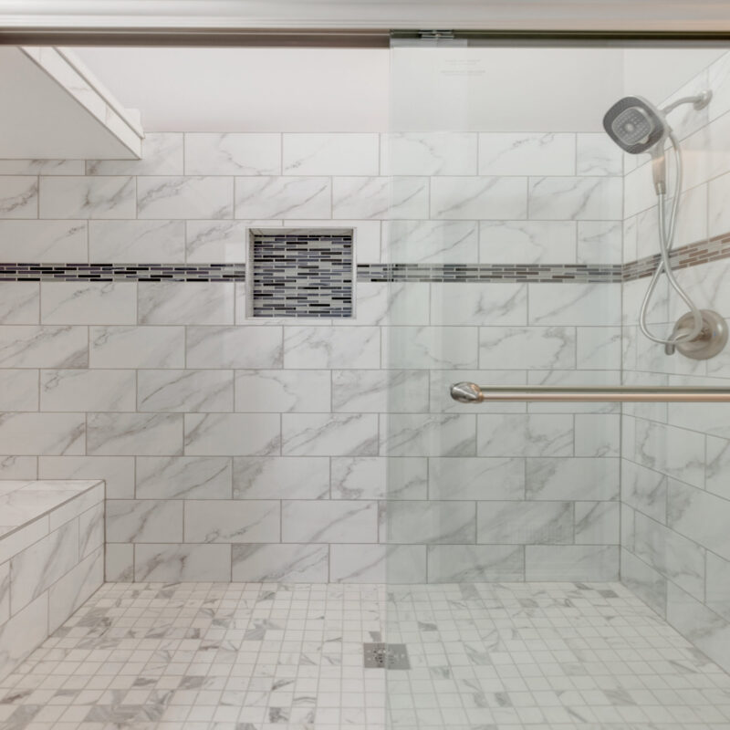 Walk-in shower with marble-look tile, mosaic accent band and niche