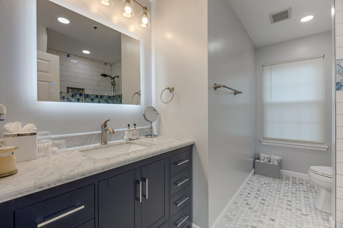 Navy vanity with marble top, backlit mirror and basketweave tile floor