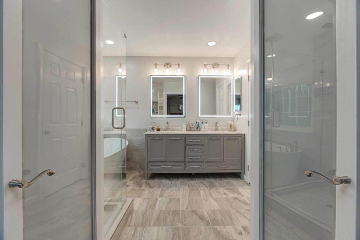 Primary bathroom with gray double vanity seen through glass shower doors