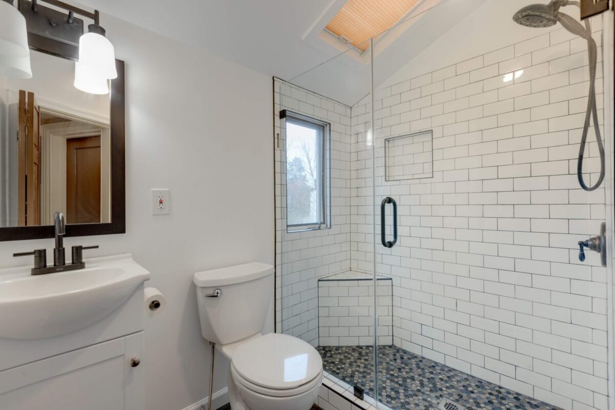 Bathroom with white subway tile shower, pebble floor and pedestal sink