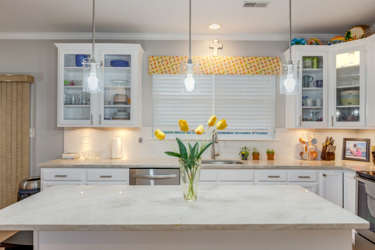 White kitchen with glass-front cabinets, marble island and pendant lights