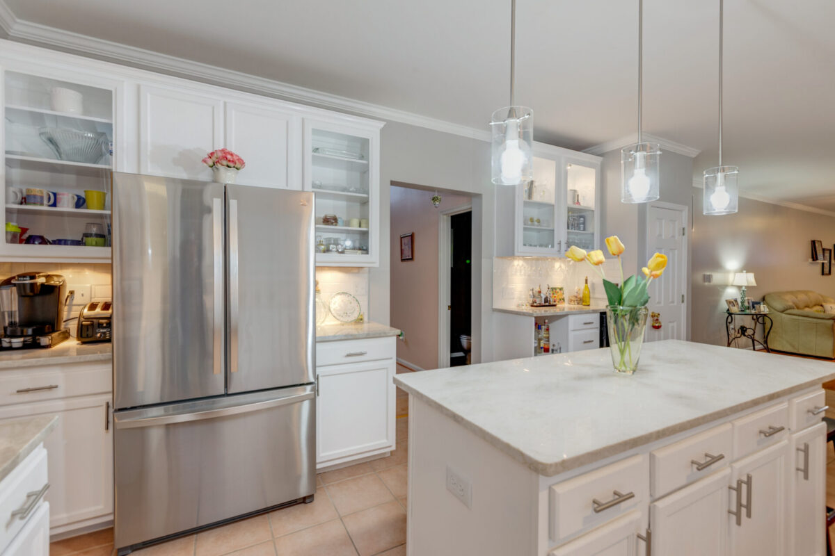 White kitchen with stainless refrigerator, island and pendant lights