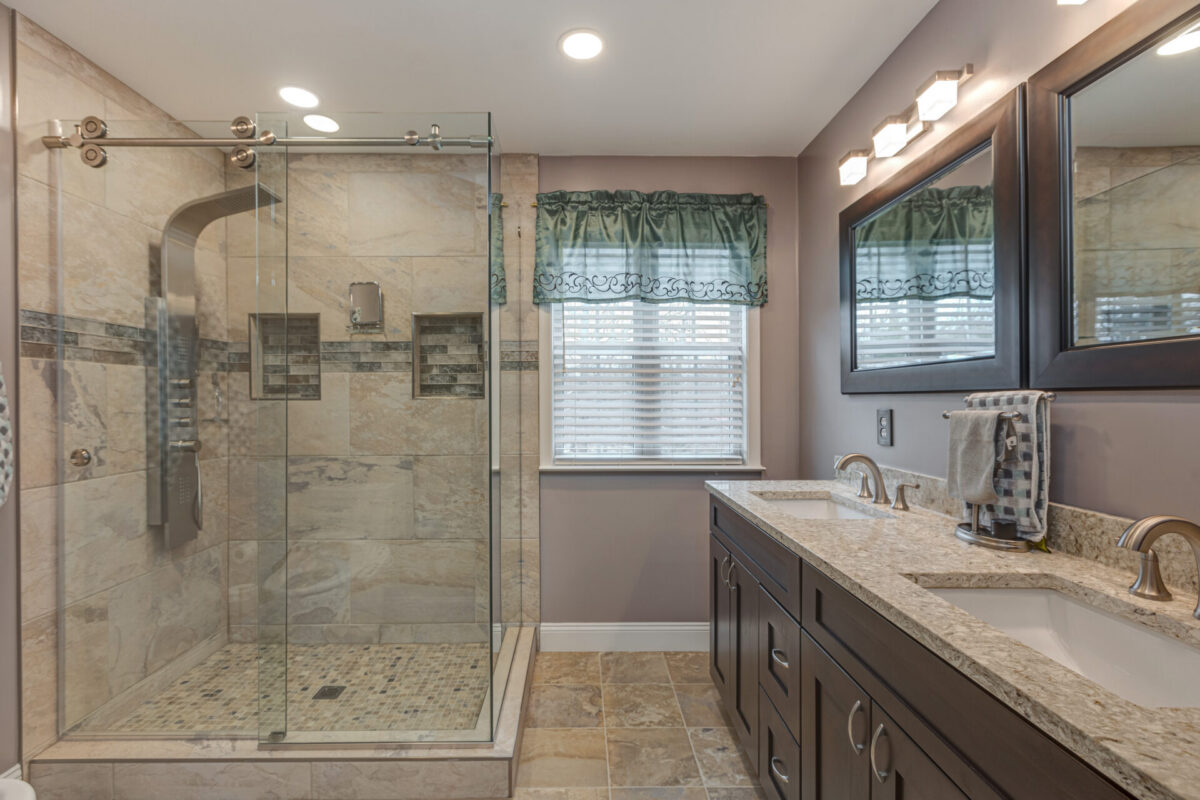 Bathroom with glass shower, tile shower panel and dark double vanity