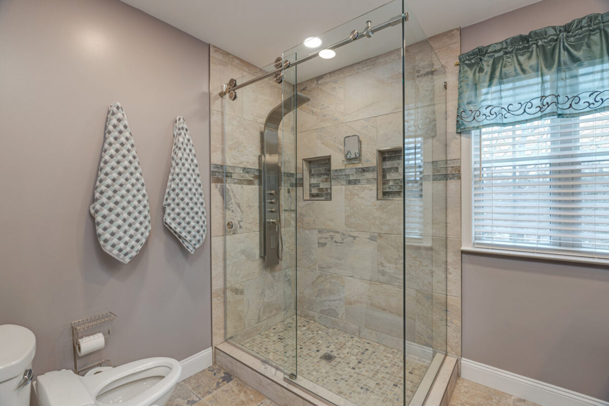 Glass shower enclosure with beige tile, mosaic band and shower panel