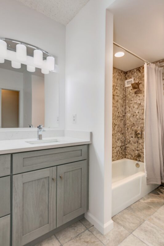 Gray vanity next to a tiled tub and shower