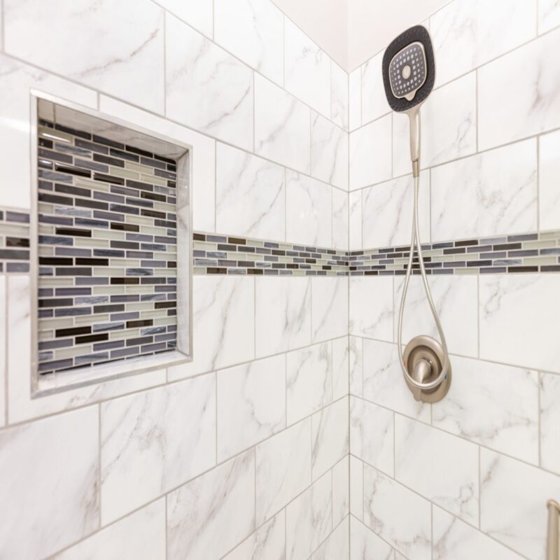Marble-look tile shower with glass mosaic niche and accent band