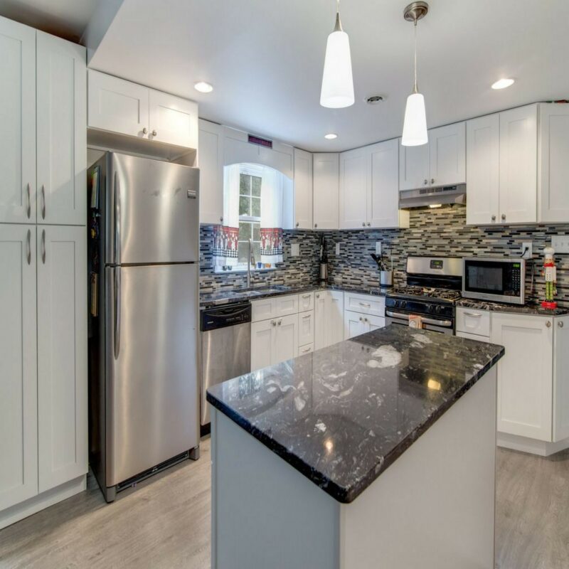 Small white kitchen with black granite island, stainless appliances and mosaic backsplash