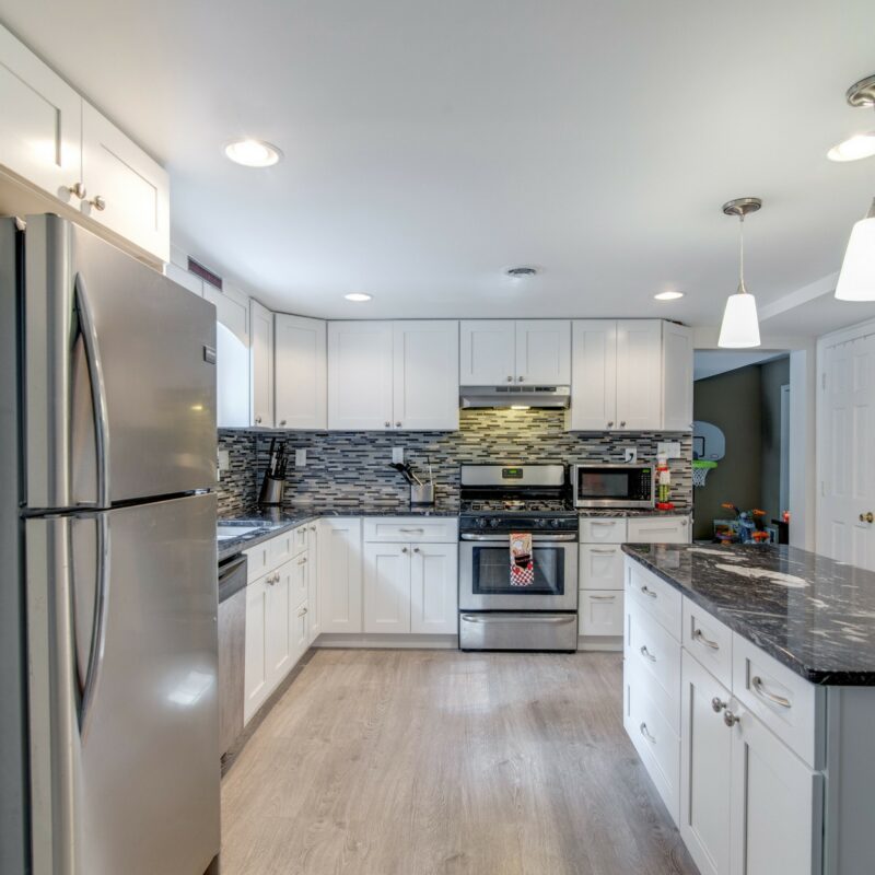 White kitchen with black granite counters, mosaic backsplash and stainless appliances