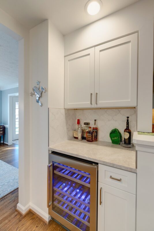 Built-in wine fridge with white cabinets and marble backsplash