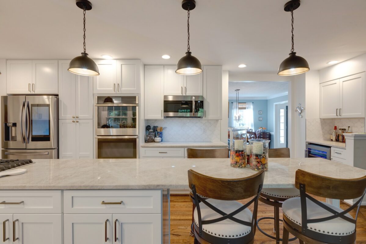 White kitchen with island stools, black pendant lights and stainless appliances