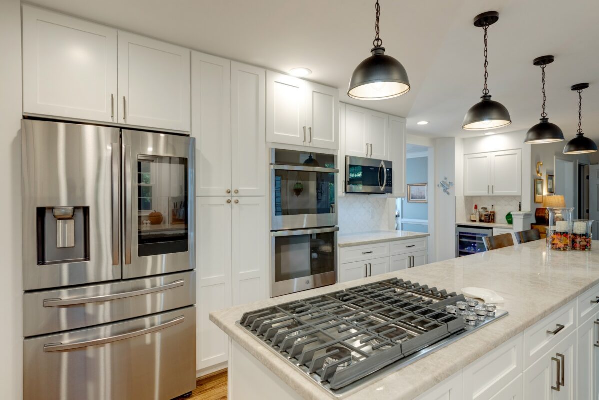 Stainless French door refrigerator and gas cooktop island in a white kitchen